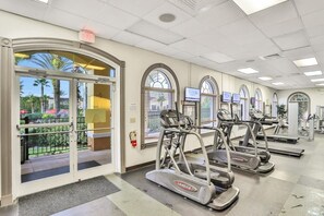 A fitness center with treadmills, a fire extinguisher, and a view of palm trees outside. - Modern 4br Home In Regal Palms Resort Near Disney 4 Bedroom Townhouse (Davenport)
