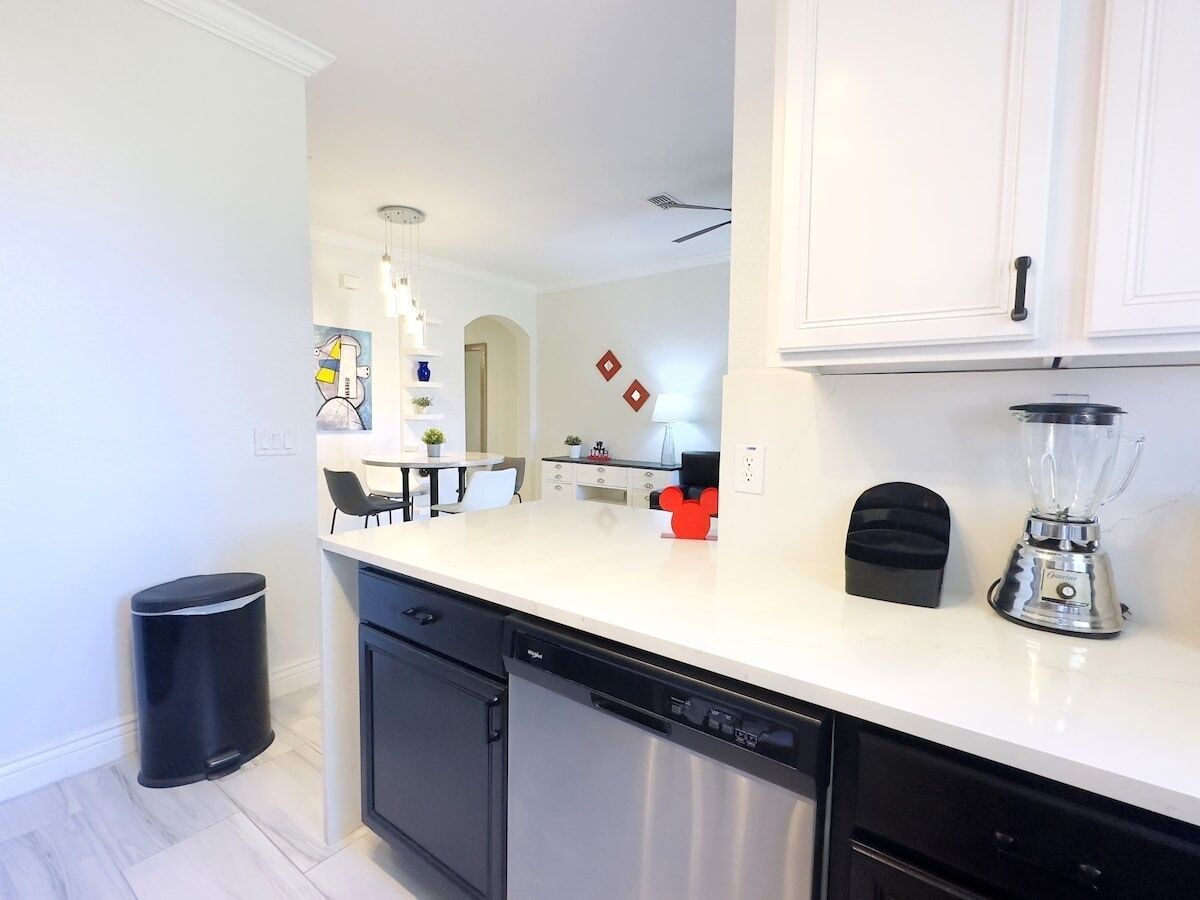 A modern kitchen with white cabinets, a dishwasher, a blender, and a trash can.