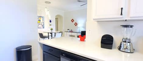 A modern kitchen with white cabinets, a dishwasher, a blender, and a trash can.