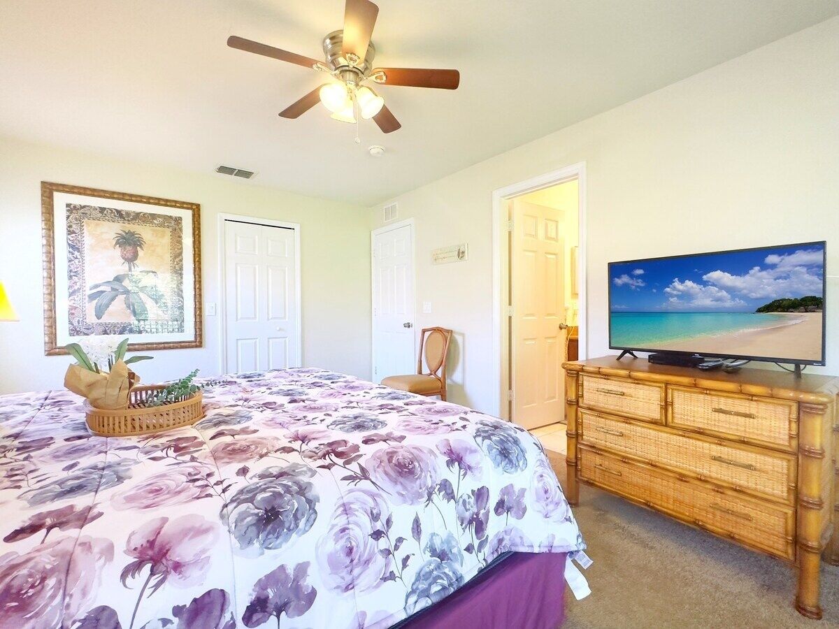 A bedroom with a bed, a television on a dresser, a ceiling fan, and a door.