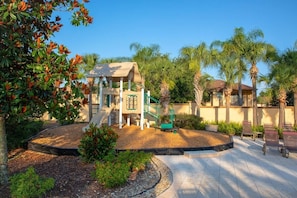 A playground with a climbing structure, surrounded by palm trees and a building with a beige facade. - 4br Resort Home With Pool And Lazy River Sleeps 10 4 Bedroom Townhouse (Davenport)