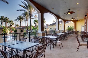 An outdoor patio with tables and chairs, palm trees, and a view of a building in the background. - 4br Resort Home With Pool And Lazy River Sleeps 10 4 Bedroom Townhouse (Davenport)