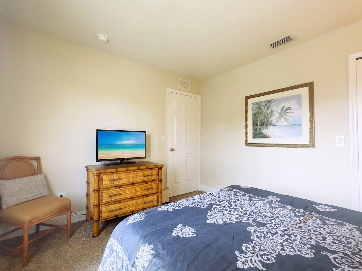 A bedroom with a bed, a television on a dresser, a chair, and a door.