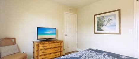 A bedroom with a bed, a television on a dresser, a chair, and a door.