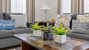 A living room with a grey sofa, a coffee table with potted plants, and a lamp in the background. - 4bd Villa Near Epic Universe And Disney With Private Pool 4 Bedroom Townhouse (Kissimmee)
