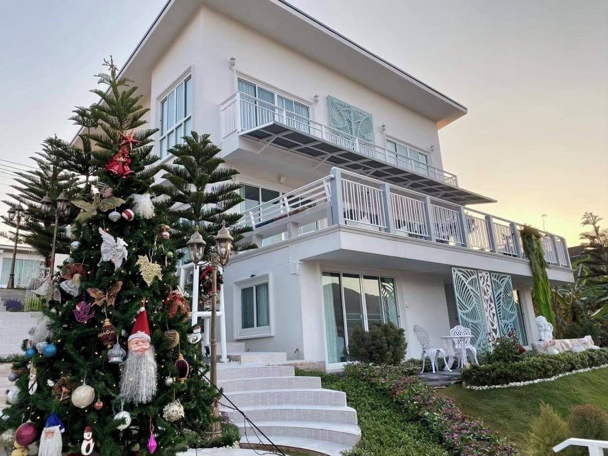A modern two-story house with a balcony, a large Christmas tree, and a well-maintained lawn.