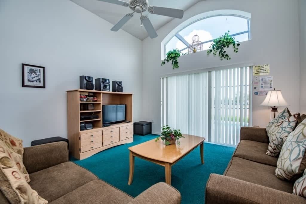 Un salon moderne avec un ventilateur de plafond, un téléviseur posé sur un meuble en bois, une table basse et un canapé.