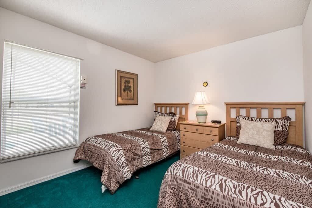A bedroom with two beds, a nightstand, a lamp, a framed picture, and a window with blinds.