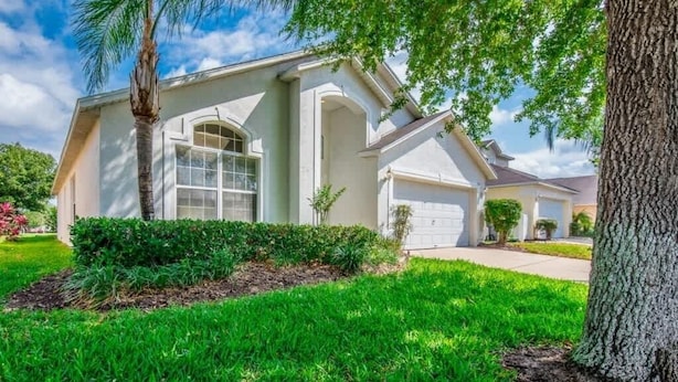 A single-story house with a front garage, a well-maintained lawn, and mature trees. - Villa Near Disney 4 Bd 3 Bt With Private Pool Quiet Comminuty 4 Bedroom Home (Davenport)