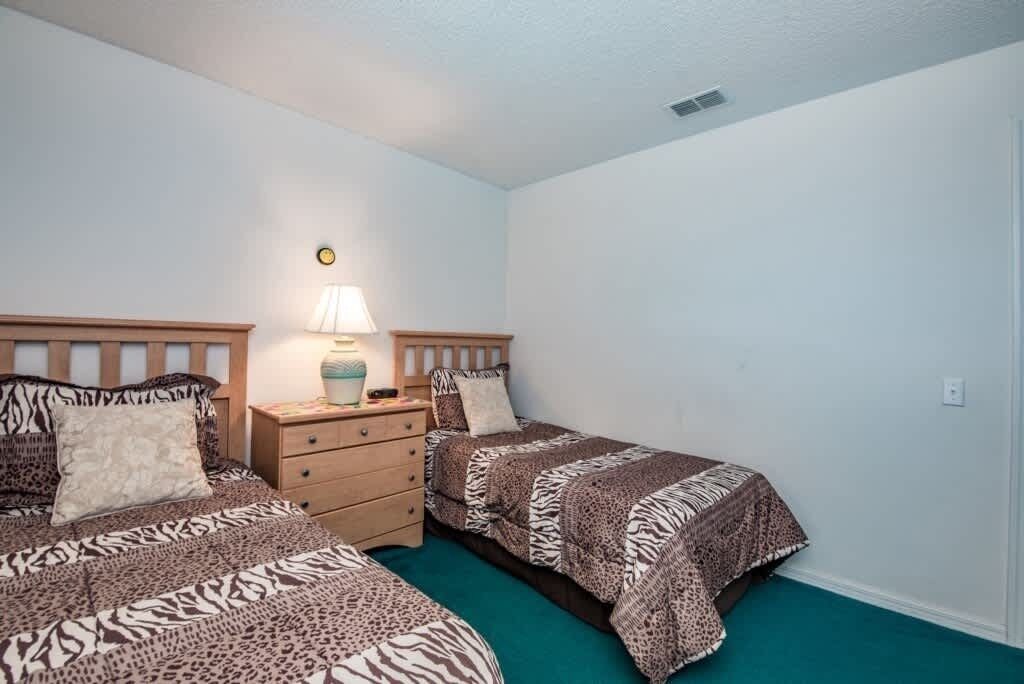 A bedroom with two beds, each with a zebra print bedspread, a bedside table with a lamp, and a small dresser.