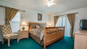 A bedroom with a wooden bed, two bedside tables with lamps, a chair, a ceiling fan, and a television on a cabinet. - Villa Near Disney 4 Bd 3 Bt With Private Pool Quiet Comminuty 4 Bedroom Home (Davenport)