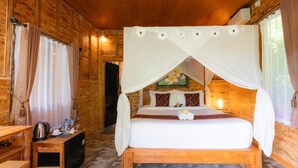A wooden cabin room with a bed under a canopy, a small table with a kettle and bottles, and a window with curtains. - Room-jungle Breeze Hideout (Ubud)