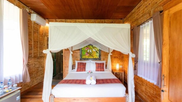 A wooden cabin-style room with a four-poster bed, a mural on the wall, and a small bedside table with a lamp. - Room-jungle Breeze Hideout (Ubud)