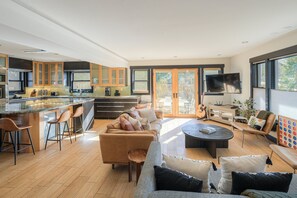 A modern kitchen with a central island, bar stools, and a dining area with a sofa and coffee table. - NEW Skyfall Haus Duo - 6BR Ultimate Downtown Pad - Locally-Managed! (Breckenridge)