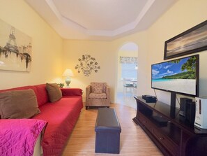 A living room with a red sofa, a patterned armchair, a coffee table, a TV, and a console table with a TV and speakers. - 4bd Pool Villa In Calabay Parc Close To Disney Sleeps 8 4 Bedroom Home (Haines City)