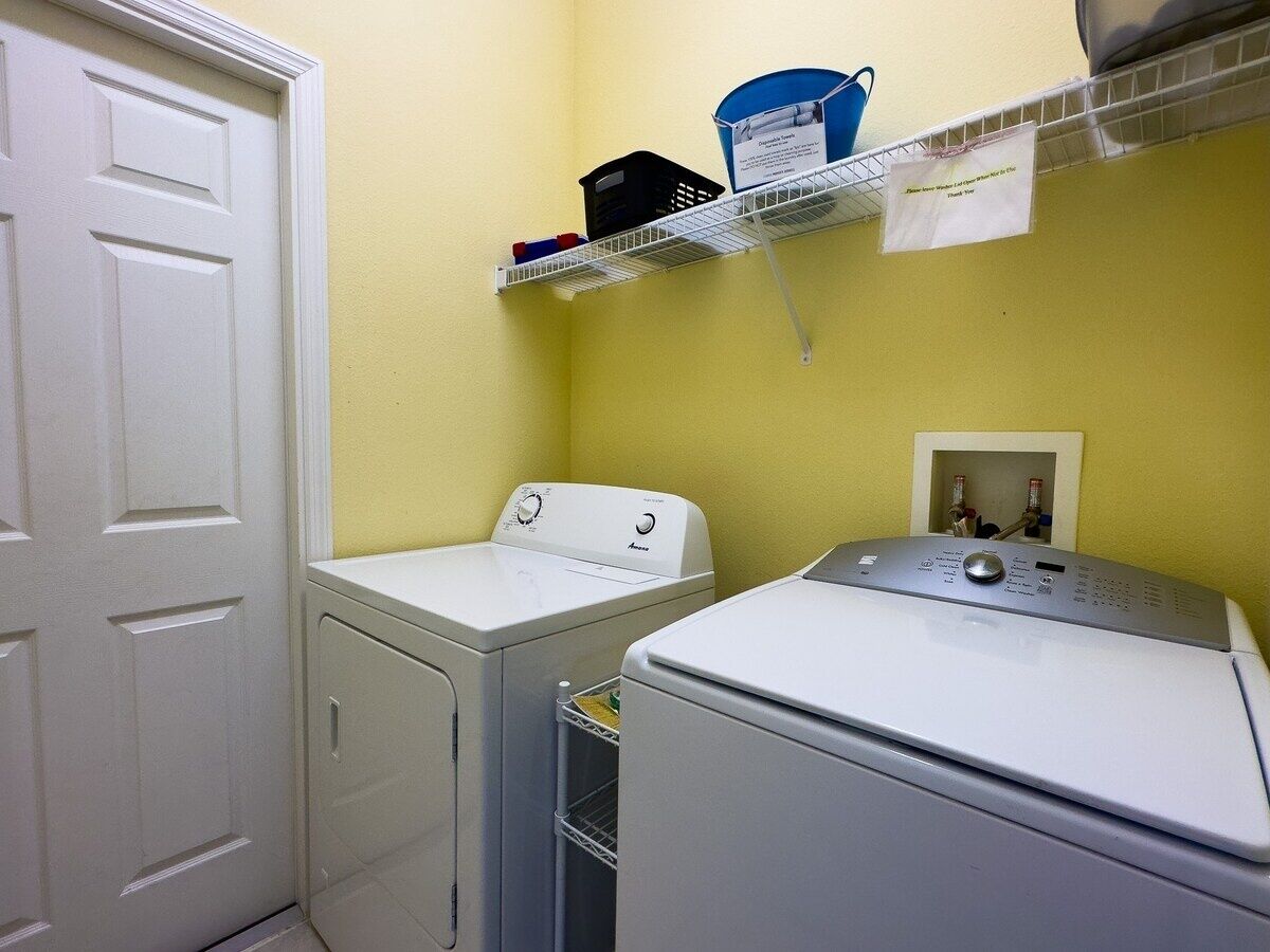 A laundry area with two washing machines, a shelf with laundry supplies, and a door.
