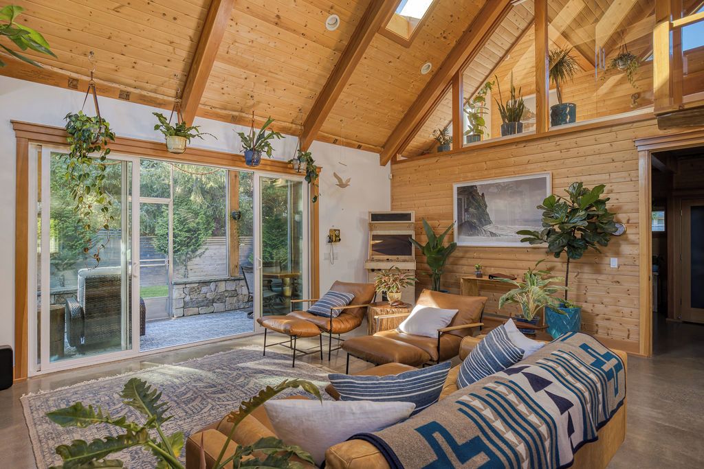 A spacious living room with a high ceiling, wooden walls, and a large sliding glass door leading to an outdoor area.