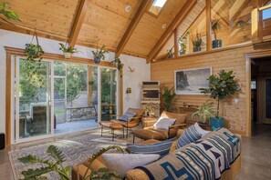 A spacious living room with a high ceiling, wooden walls, and a large sliding glass door leading to an outdoor area.