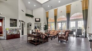 A spacious lobby with a reception desk, seating area with wicker furniture, and large windows with curtains. - Luxury Villa Near Disney 6 Bd Home With Private Pool And Resort 6 Bedroom Home (Davenport)