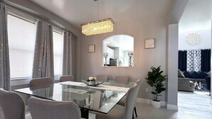A dining area with a glass table, cushioned chairs, a chandelier, and a potted plant. - Luxury Villa Near Disney 6 Bd Home With Private Pool And Resort 6 Bedroom Home (Davenport)