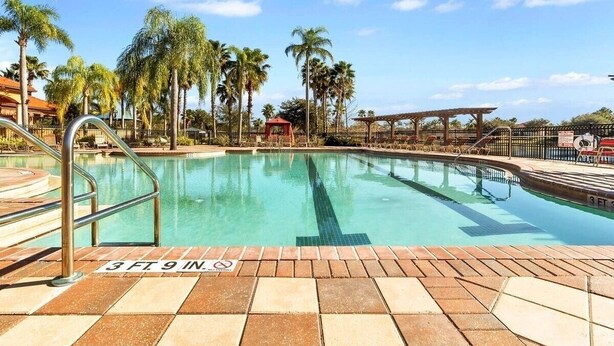 A swimming pool with a 3 FT 9 IN depth marker, surrounded by palm trees and a covered seating area. - Luxury Villa Near Disney 6 Bd Home With Private Pool And Resort 6 Bedroom Home (Davenport)