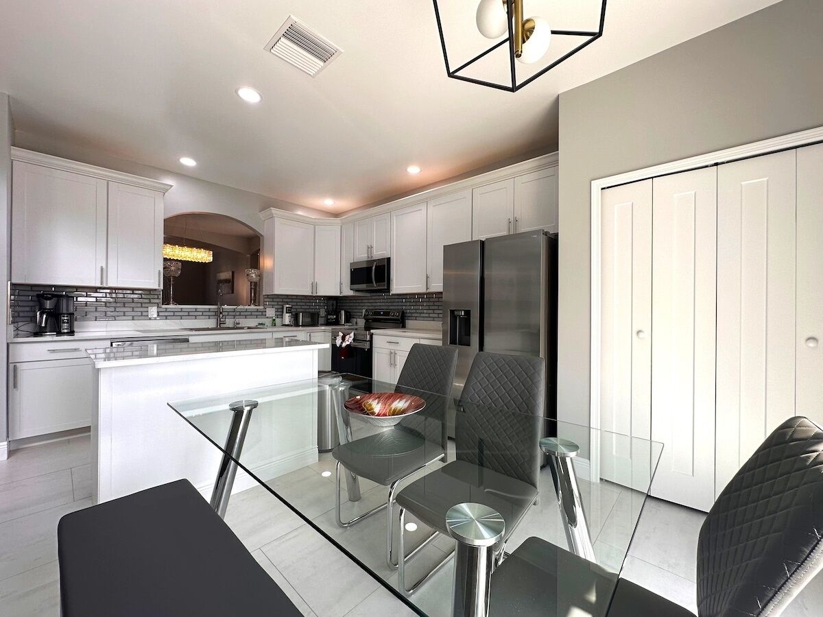 A modern kitchen with white cabinetry, a glass dining table, and a stainless steel refrigerator.
