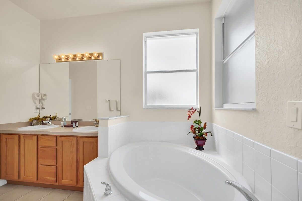 A bathroom with a large bathtub, wooden cabinets, a vanity with a mirror, and a window.