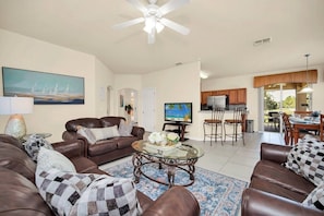 A spacious living area with a brown leather sofa, a glass coffee table, and a television. - Near Disney Amazing 5 Bd Home - Private Pool 5 Bedroom Home (Davenport)