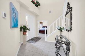 A hallway with a white door, a potted plant, a painting, a glass table with a vase, and a staircase with a white railing. - Near Disney Amazing 5 Bd Home - Private Pool 5 Bedroom Home (Davenport)
