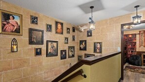 Un pasillo con pared de ladrillo, barandal de madera y una serie de cuadros enmarcados.