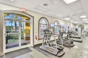 Ein Fitnessstudio mit Laufbändern, Trainingsgeräten und Blick auf Palmen draußen.