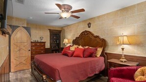 Un dormitorio con una cama de madera, un ventilador de techo, un sillón tapizado de color rojo y un armario de madera.