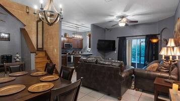 A modern living room with a dark leather sofa, a dining table with plates, and a chandelier.