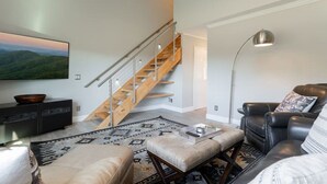 Een moderne woonkamer met een trap, een leren bank en een flatscreen televisie.