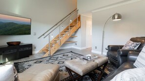 A modern living room with a staircase, leather sofa, and a flat-screen TV. - Lake Lure Getaway | Lake Lure Condo Inside Rumbling Bald Resort | Pools, Beach Access + Golf (Lake Lure)