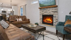 Een moderne woonkamer met een stenen openhaard, leren banken en een flatscreen televisie erboven.