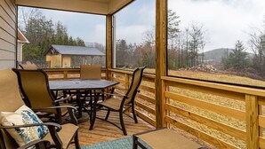 Een overdekt buitengebied met een houten terras, een tafel en stoelen.