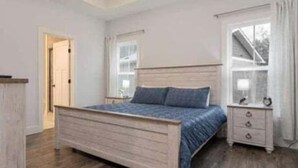 Een slaapkamer met een houten bed, nachtkastje, dressoir en een raam met gordijnen.