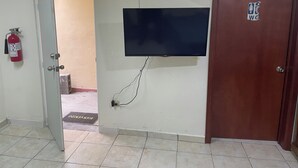 Een kamer met een betegelde vloer, een flatscreen televisie aan de muur, een houten deur en een brandblusser aan de muur.