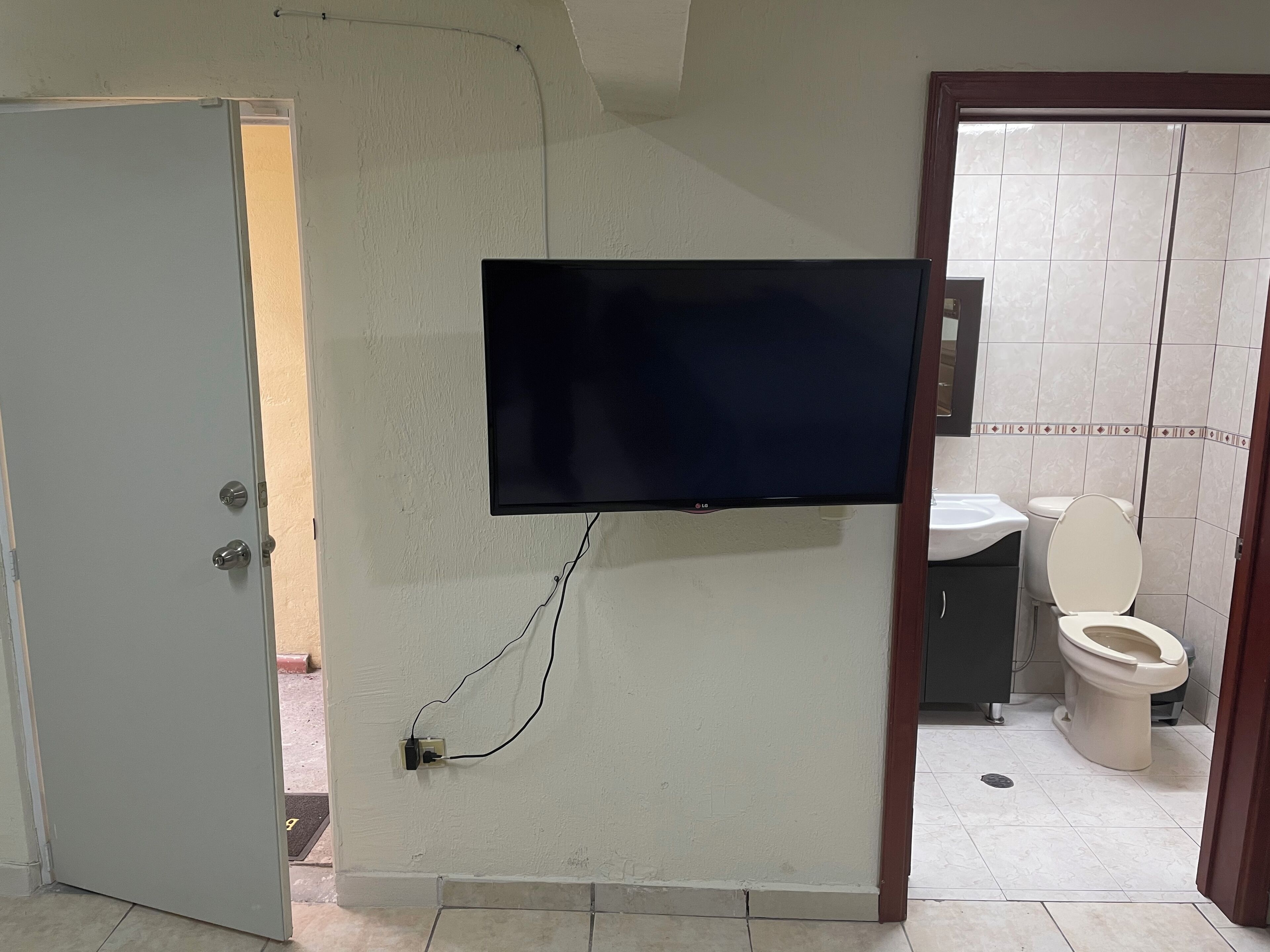 Casa de banho com sanita, lavatório e televisão de ecrã plano fixada na parede.