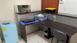 Een compact keukenhoekje met een magnetron, een kleine koelkast en een kookplaat.