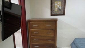 Een kamer met een houten dressoir, een bed met een blauwe spreidek en een ingelijst foto aan de wand, plus een aan de muur bevestigde televisie.