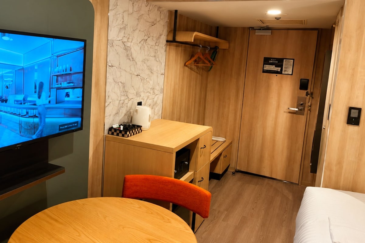 Una habitación de hotel con un escritorio de madera, televisor, cama y pared de mármol.