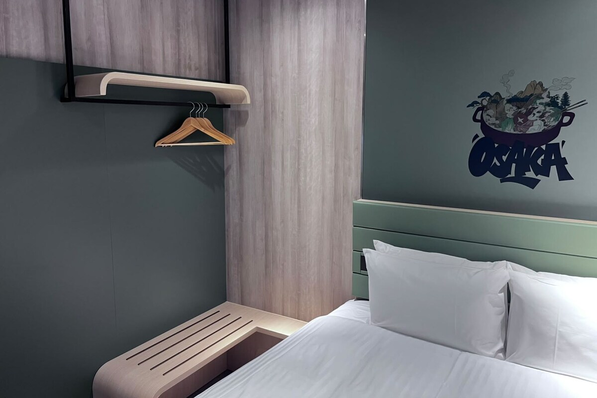 Una habitación de hotel moderna con una cama, un banco de madera, un estante en la pared y una decoración mural.