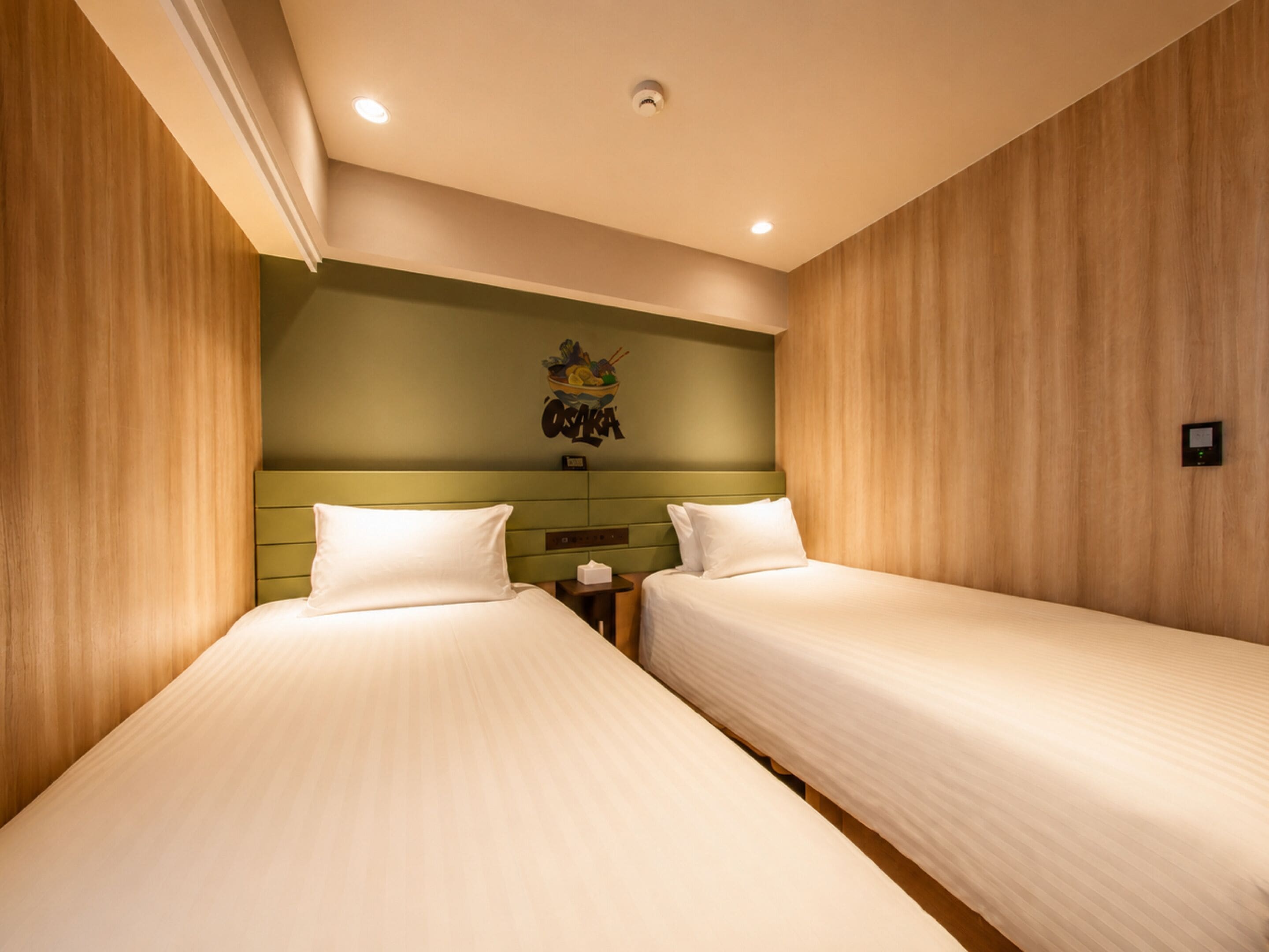 Una habitación de hotel con dos camas individuales, un cabecero verde y una obra de arte colgada en la pared.