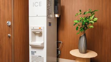 Ein weißer Eisschrank mit Wasserspender, ein kleiner Tisch mit einer Vase grüner Pflanzen und eine Holztür.