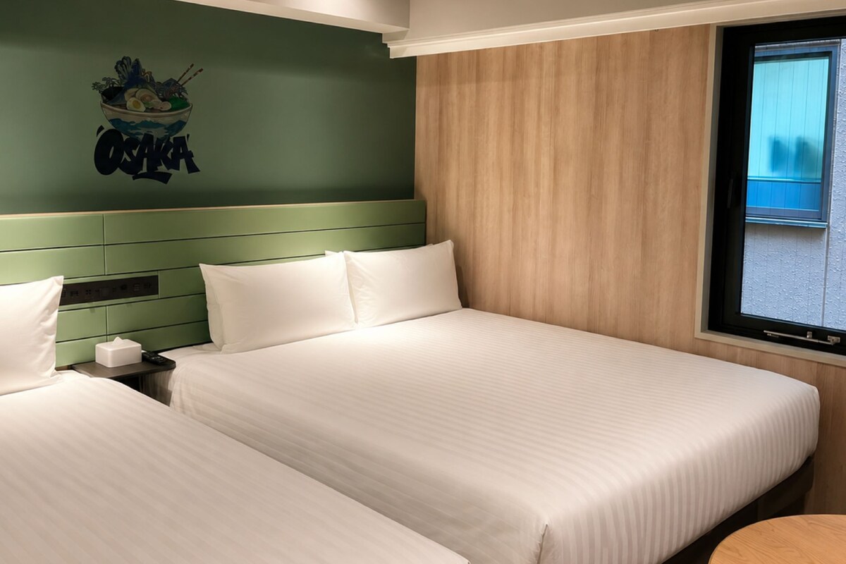 Una habitación de hotel con dos camas, una pared de acento verde, un revestimiento de madera y una ventana con vistas.