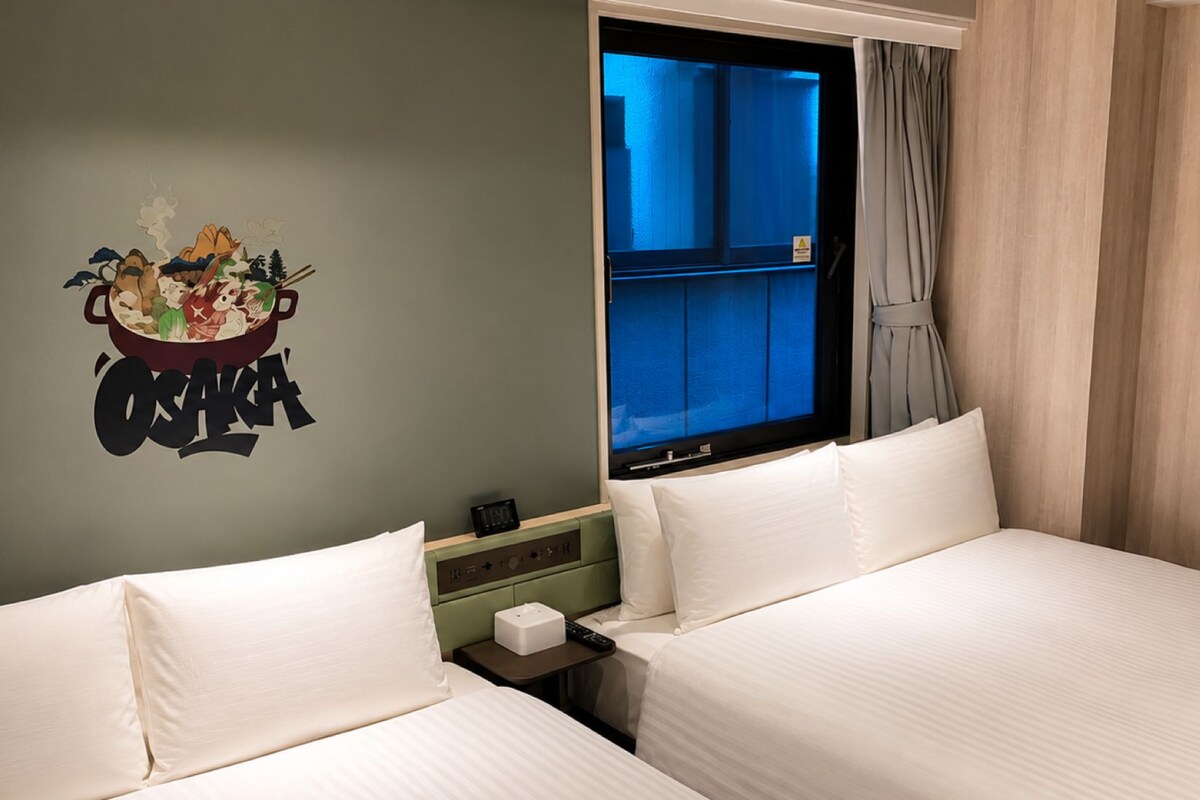 Habitación de hotel con dos camas, una decoración en la pared, una ventana y una mesita de noche.