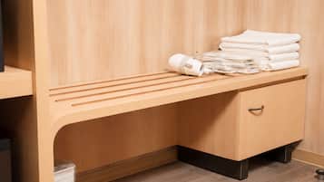 A wooden bench with towels and a hairdryer, a wooden cabinet with a drawer, and a trash bin.