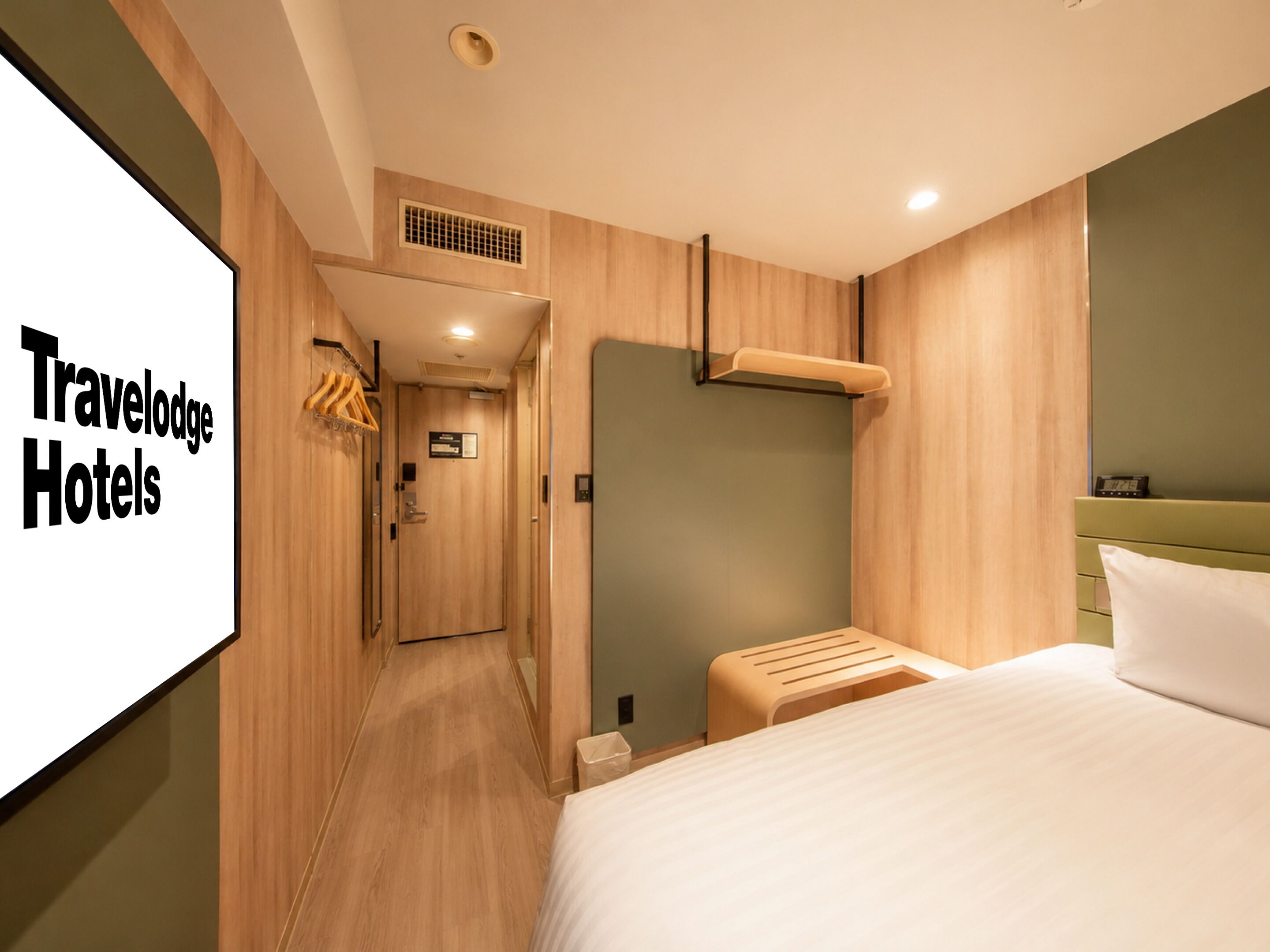 A modern hotel room with a wooden floor, a bed with white bedding, a small bedside table, a wall-mounted heater, and a wardrobe with a mirror.